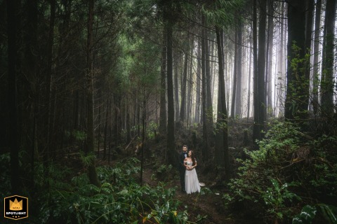 The couple poses together in a fog-covered forest in the Azores, Portugal, surrounded by mist and towering trees that create a dramatic and atmospheric wedding-day setting.