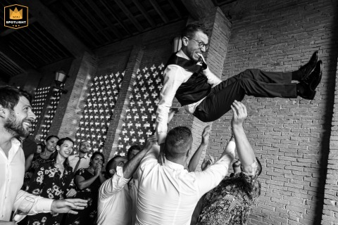 During the reception at Agriturismo Costavecchia in Ghisiolo, Mantua, Italy, the groom is thrown into the air by friends, creating a lively and celebratory scene.