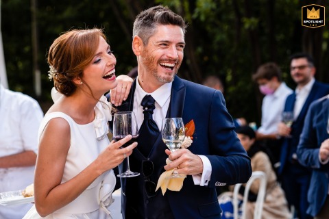 The bride and groom laugh together during the aperitif at Castelvecchio in Sagrado, Gorizia, Italy, enjoying a relaxed and joyful part of their wedding celebration.