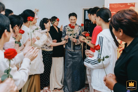 In Kaifeng, Henan, China, the groom appears while friends offer flower-filled blessings, greeting him with lively celebration and cheerful anticipation for the wedding festivities.