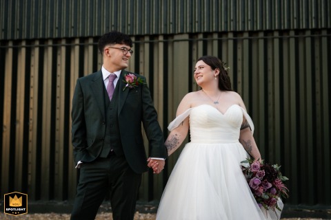 A bride and groom pose for a portrait outside Tythe Barn, standing close together beside the rustic venue on a quiet wedding afternoon, smiling there.