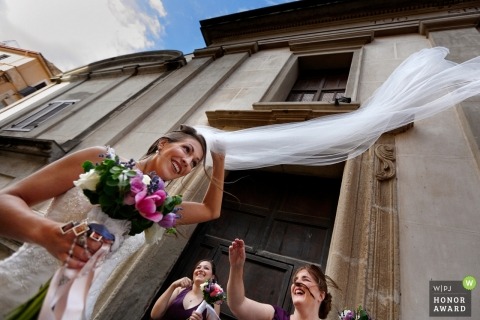 Bridesmaids and bride trying to stop the vale from flying away in this Reggio Calabria wedding photo