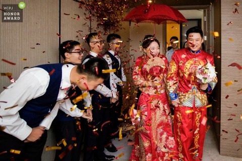 Fujian wedding photojournalism image of a couple dressed in red with a red umbrella as confetti flies