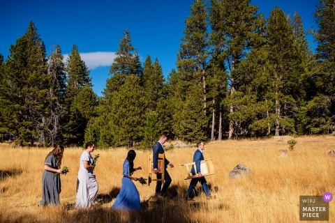 Lake Tahoe wedding photo | wedding photograph of pre-ceremony of guests walking across field carrying chairs