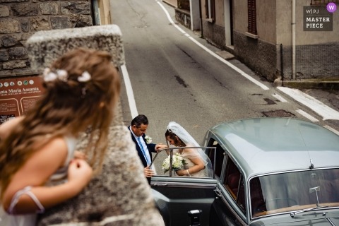 Italy wedding Image of a bride exiting a vintage limousine as seen from the perspective of a young flower girl on the second floor