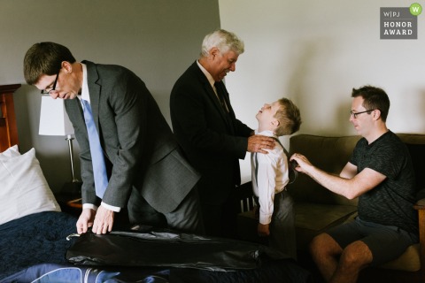 An exceptional Dundee NY wedding image by a pro New York photographer at the Glendora Wine Cellar exhibiting A grandfather exchanging a happy look with his grandson while the boys father fixes the boys suspenders and an uncle prepares