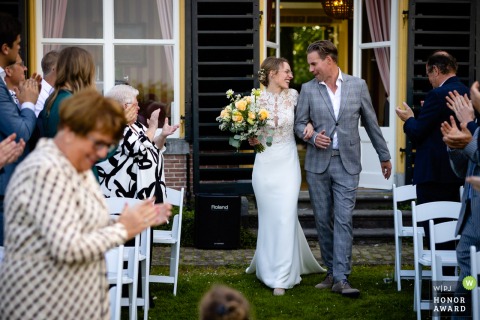 De bruid en haar vader lopen door het gangpad van de buitenceremonielocatie, huis brakel