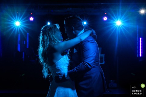 In East Flanders, Belgium, the couple shares their first dance under blue DJ lights at a party.