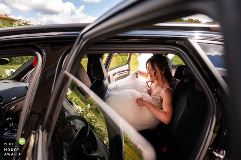 A bride, wearing a white wedding gown, enters a car in Udine, Italy, on her wedding day.