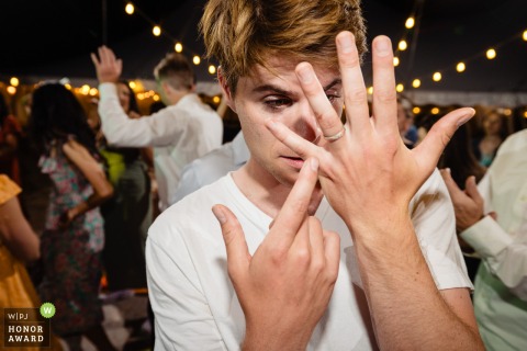 Groom Inspects Ring During Lively Reception in Durango, Colorado, Sporting a Casual Undershirt Look In Durango, Colorado, the groom, wearing his undershirt amidst the lively party scene, closely examines the ring on his finger.