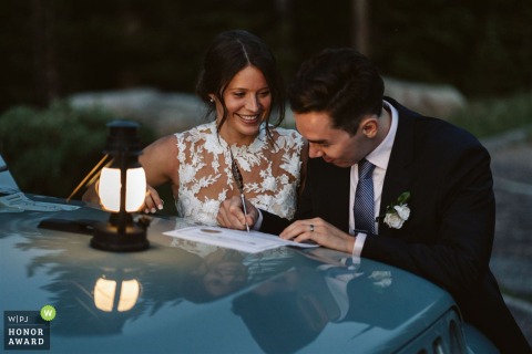 In Indian Peaks Wilderness, CO, a couple signs their marriage license on the hood of their Jeep after eloping, illuminated by a lantern at dusk.