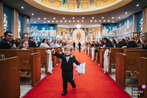 At a Cleveland, Ohio wedding ceremony, the ring bearer hesitates midway down the aisle, uncertain, while guests watch curiously.