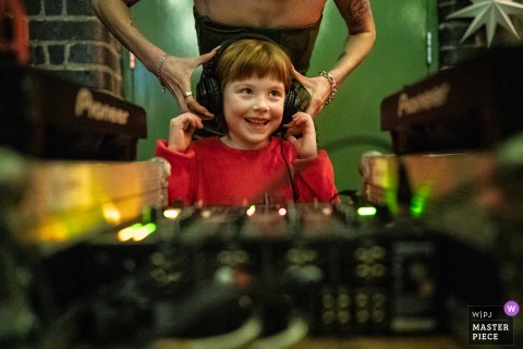 London Wedding Groove: Young DJ with Headphones Steals the Show In London, UK, a young child wears headphones and stands at the DJ booth during the wedding party, entertaining guests.