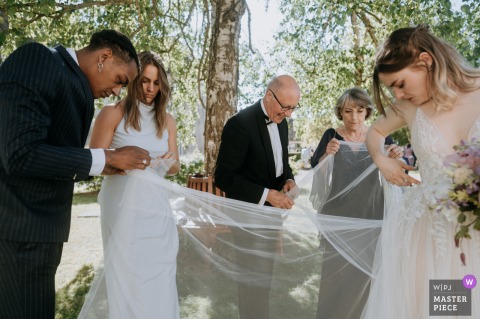 Joyful Chase at Le Clos: Playful Wedding Antics Beneath the Bride’s Dress At Le Clos Barisseuse, Hauts de France, family members joyfully chase bugs beneath the bride’s dress, creating a playful wedding moment.