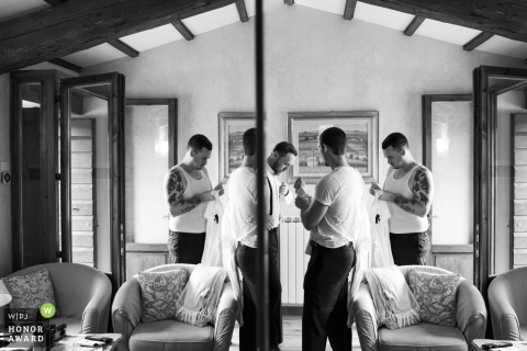 Groom and friends prepare for the ceremony, reflected in a mirror creating near-perfect symmetrical balance within their hotel room interior.