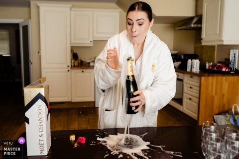 Bride laughs as she accidentally spills champagne while getting ready at Kilkea Castle, Kildare, Ireland, capturing a candid wedding moment.