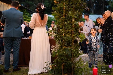 At a wedding reception in Cagliari, Sardinia, a child joyfully plays with bubbles, ignoring the imminent cake cutting ceremony.