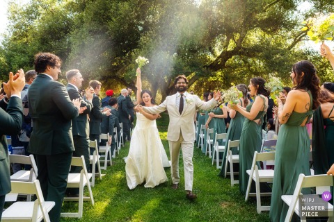 At Milagro Winery in Ramona, CA, the bride and groom joyfully walk down the aisle together as newlyweds.