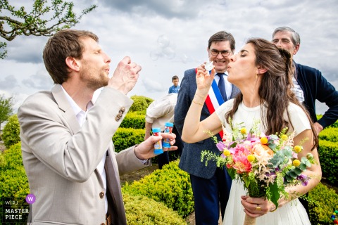 In front of Puycornet town hall, the newlyweds joyfully blow soap bubbles together, celebrating after their wedding ceremony.