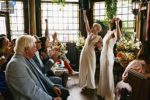 At The Prince Albert pub in Camden, London, elated brides celebrate after their ceremony, joyfully cheered on by guests.