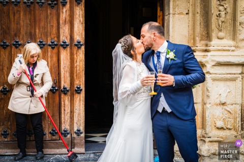 Newlyweds, beaming with joy, exit Basílica de San Ildefonso as caretaker clears path gently.