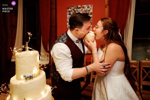 At their Fribourg, Switzerland reception, the bride and groom hilariously bite directly into their wedding cake, sharing joyful laughter.