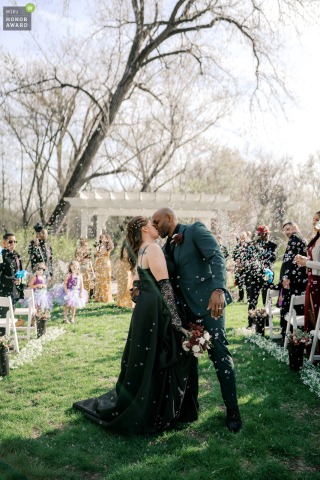   In a joyful scene at Hidden Creek Estates in Roscoe, Illinois, the bride and groom pause for a kiss as guests blow bubbles while they walk back up the aisle.