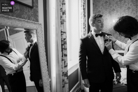 The groom’s brother delicately pins the boutonniere on his suit, reflected in a beautiful mirror at The Madison Club.