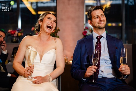   During heartfelt speeches at The Rally Hotel in Denver, Colorado, the bride and groom share a genuine laugh, surrounded by friends and family.
