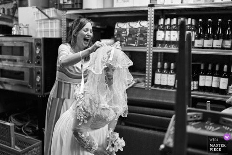 Bride receives a quick veil adjustment in the storage area of the Amsterdam Noord Holland reception venue, candid wedding preparation moment.