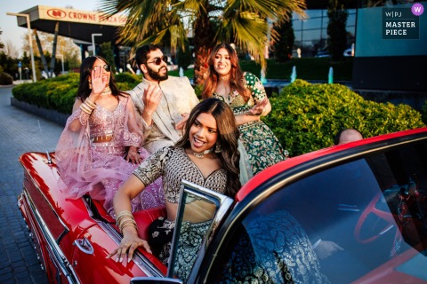 Groom arrives at Crowne Plaza Hotel, Istanbul, in a classical car during vibrant Baraat procession, guests joyfully celebrating.