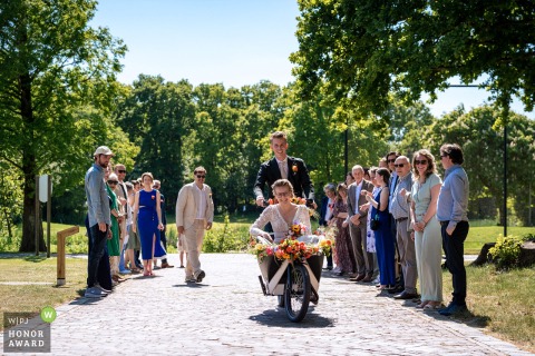   The wedding couple arrives together by bicycle, a special surprise organized by the masters of ceremony, making a memorable entrance at the venue in Zuid Holland.