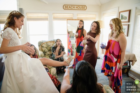   Friends gather around the bride in Duck, North Carolina, reacting enthusiastically as she proudly shows off her wedding shoes.