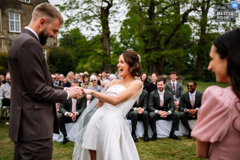 At Talton Lodge, Warwickshire, the bride laughs joyfully during the exchanging of rings, capturing a candid, heartfelt wedding moment.