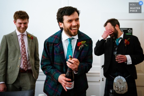 Groom and groomsmen laughing and helping each other get dressed in suits while preparing for the wedding at Temple, London.