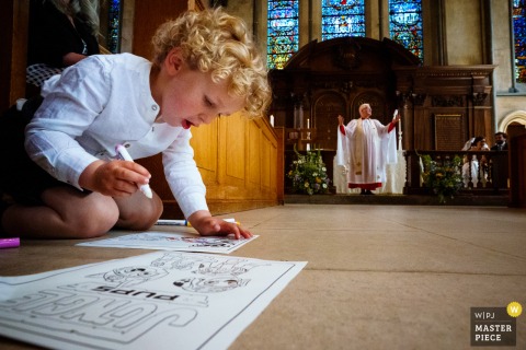 Innocent Distraction: Young Guest Engrossed with Toy During Temple Church Ceremony A young wedding guest sits quietly, distracted and occupied with a toy, during the ceremony at Temple Church, London, UK.