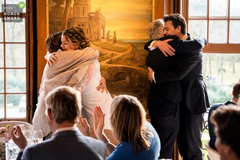   After an emotional speech at wedding venue Buitenplaats Sparrendaal, the bride and groom warmly embrace their parents in a heartfelt group hug.
