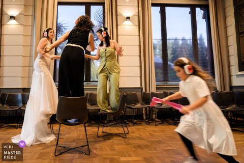 At Orangerie Hydepark, Doorn, the bride enjoys a silent disco with friends as a girl playfully runs by in front.