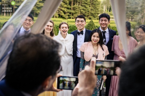  At The Mount in Lenox, Massachusetts, family members eagerly gather during cocktail hour to take group photos on their phones, preserving memories of the special day.