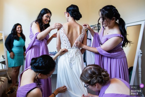 San Francisco bridesmaids gather around to help the bride put on her wedding dress.
