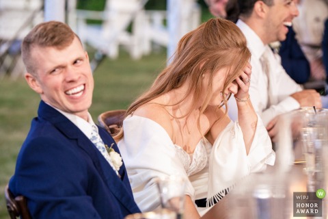 Seated at their reception at the Walled Garden in Wiscasset, Maine, the couple shares a range of candid and joyful reactions while listening to heartfelt toasts from their guests.