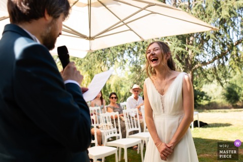 At Château de Launac in Haute-Garonne, the groom reads into a microphone, causing the bride to burst into laughter. The award-winning photograph highlights the photographer's skill at documenting candid, joyful moments.