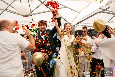 At Château de Launac in Haute-Garonne, France, the bride and groom exit holding hands overhead under a shower of petals. The award-winning photo highlights the photographer's skill at documenting pure joy.
