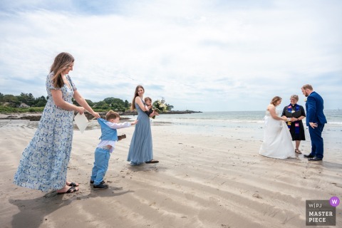 Couple's Son Tries to Join Beach Ceremony, Held Back by Aunt in Kennebunkport, Maine In Kennebunkport, Maine, the couple's son tries desperately to join the beach ceremony, held back by his aunt. The award-winning photo highlights the photographer's skill at documenting the humorous family moments.