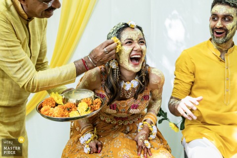 Relative Applies Turmeric and Saffron During Hindu Haldi Ceremony in Backyard on Atlanta’s Northside Drive In a backyard on Atlanta’s Northside Drive, a relative applies turmeric and saffron to a couple during a Hindu Haldi ceremony. The award-winning photo highlights the photographer’s skill at documenting vibrant traditions.