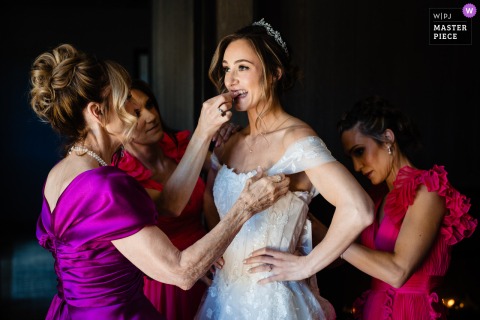 In Big Sky, Montana, a friend helps a bride remove something from her teeth as others assist with her dress. The winning photo highlights the photographer's skill at documenting funny, and genuine wedding moments.