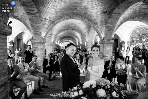 At Tenuta Borgo la Caccia in Pozzolengo, Italy, a groom playfully asks the celebrant if he can kiss the bride. The winning photo highlights the photographer's skill at documenting the charming, unscripted moments of a ceremony.