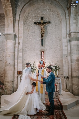 Newlyweds Exchange Vows As Daughter Hugs Them At San Basilio Church Troia Family Wedding At San Basilio church in Troia, newlyweds exchange vows as their daughter emotionally hugs them. The award-winning photo highlights the photographer’s skill at documenting the sincere, heartfelt moments of a family wedding.