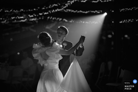At a reception venue in Mayenne, Pays de la Loire, a newlywed couple shares their first dance, a waltz. The black-and-white photo highlights the photographer's skill at documenting the timeless emotion of the moment.