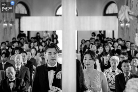 Cross Divides Newlywed Couple And Crowd At Mandarin Oriental Taipei Taiwan In Striking Wedding Composition At the Mandarin Oriental in Taipei, Taiwan, a cross in the foreground divides a newlywed couple and the crowd. The award-winning photo highlights the photographer's skill at using powerful composition to document genuine wedding moments.